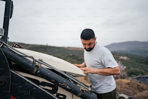 Un homme debout à côté d’un véhicule tenant une planche de surf