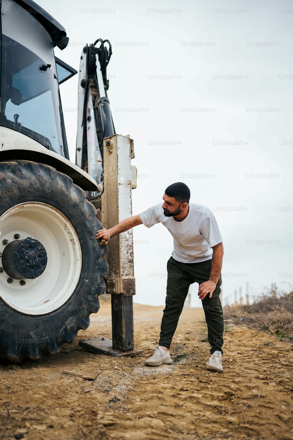Un hombre apoyado en un poste junto a un tractor