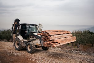 uma empilhadeira que transporta uma carga de madeira em uma estrada de terra