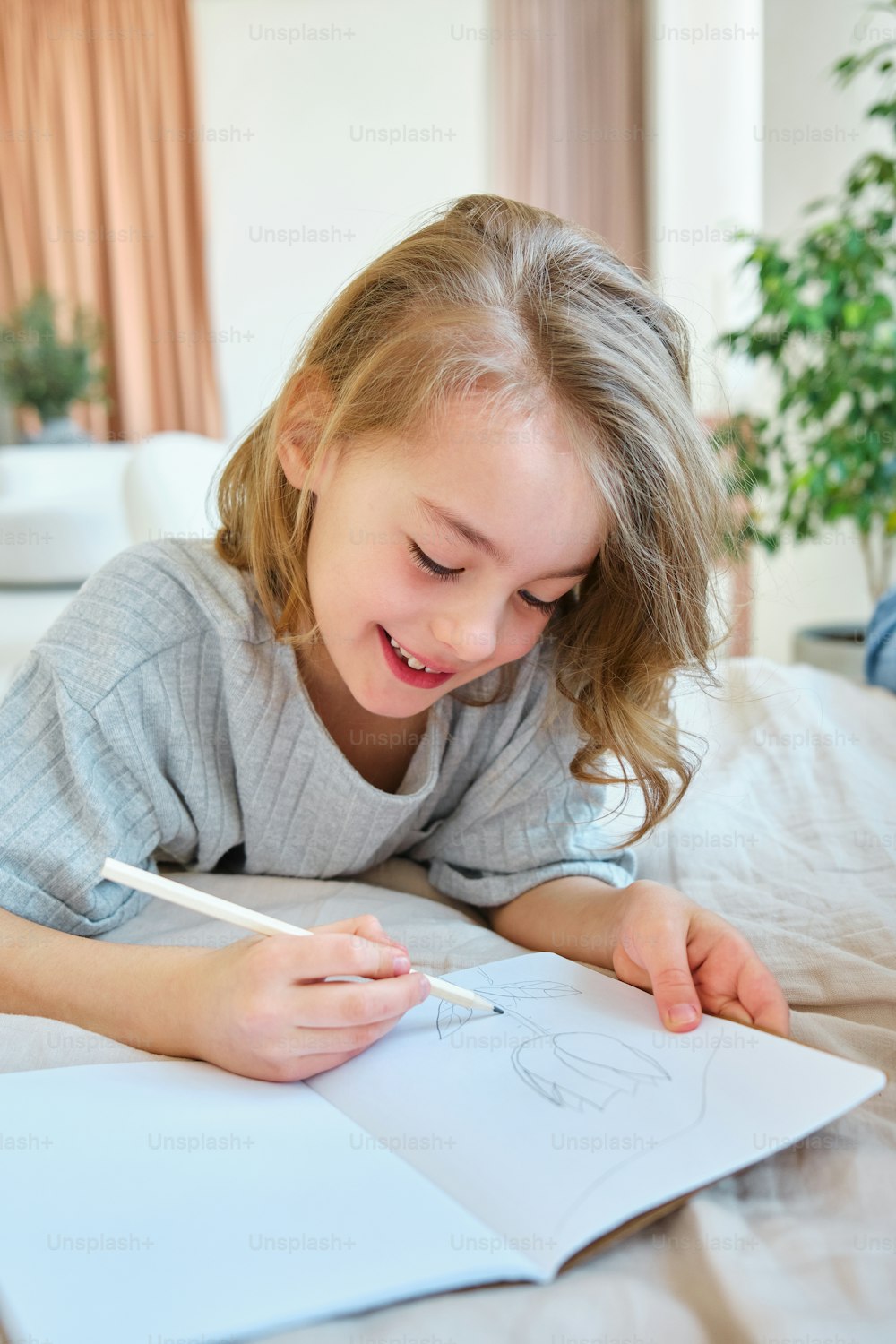 a little girl laying on top of a bed drawing