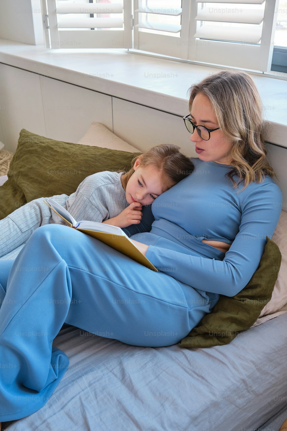 침대에서 아이에게 책을 읽어주는 여자