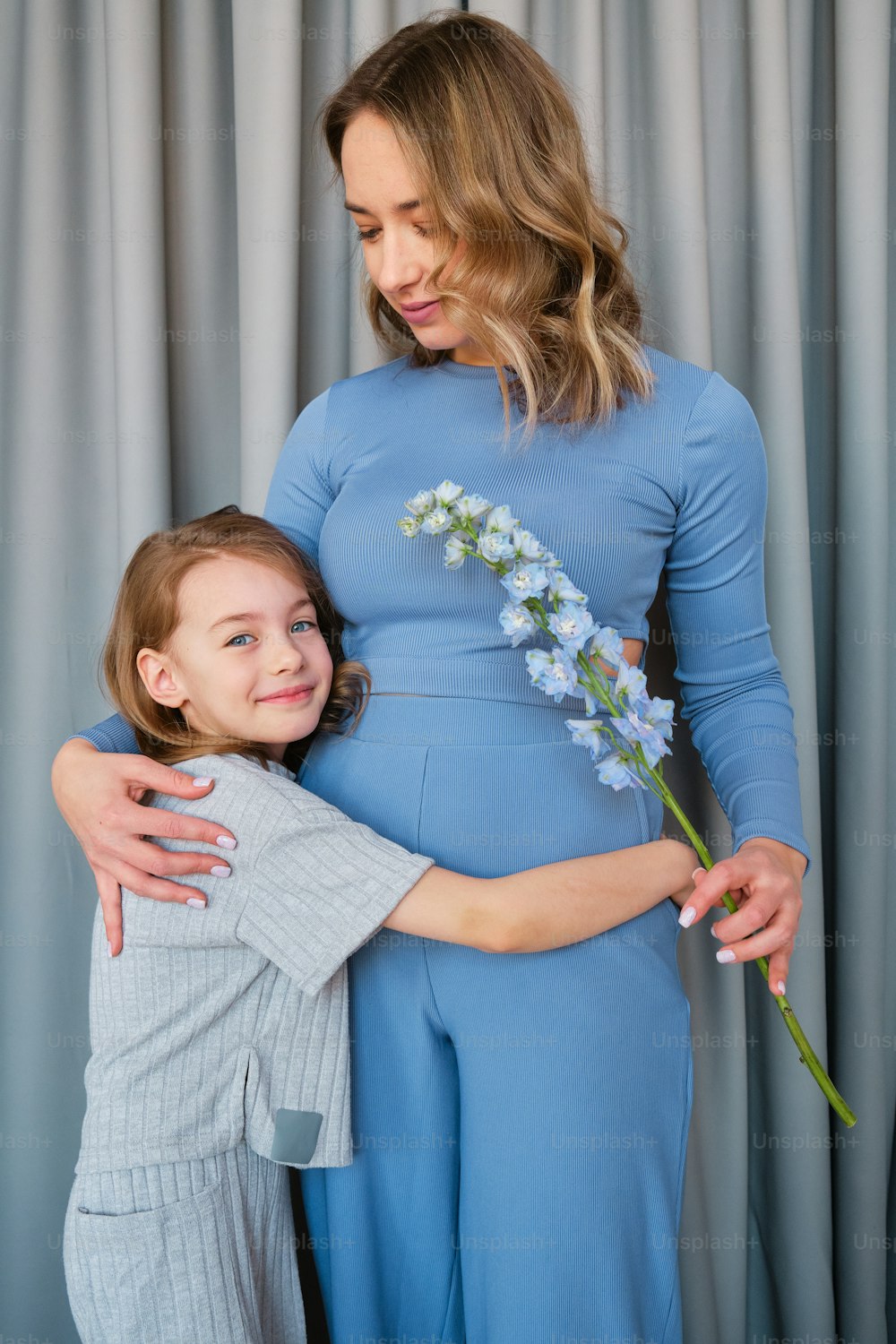 a woman is hugging a little girl who is holding a flower