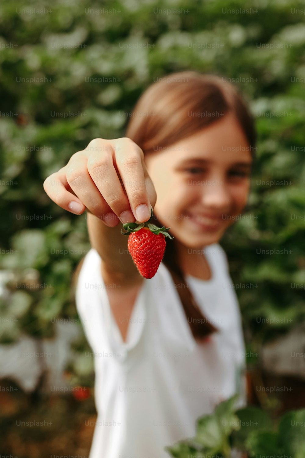 a woman holding a strawberry up to the camera