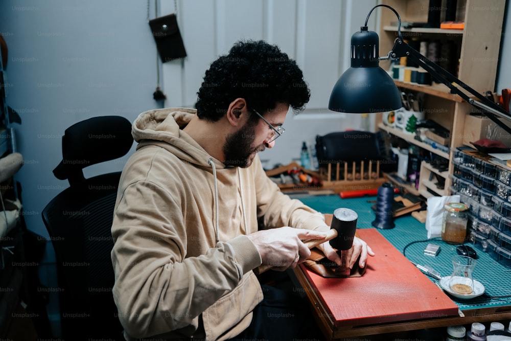 a man sitting at a desk working on a piece of wood