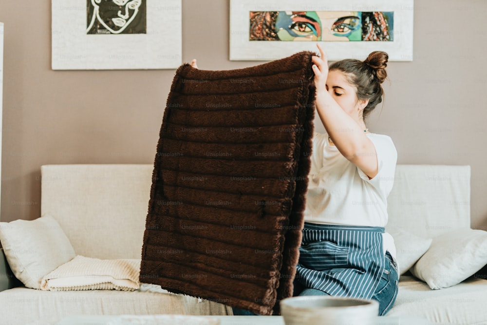 a woman sitting on a couch holding up a blanket