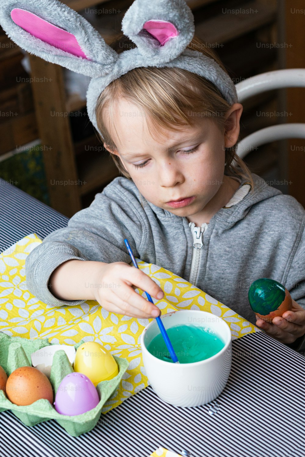 a little girl sitting at a table painting eggs