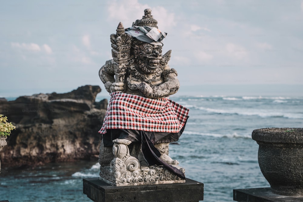 a statue sitting on top of a cement block next to the ocean