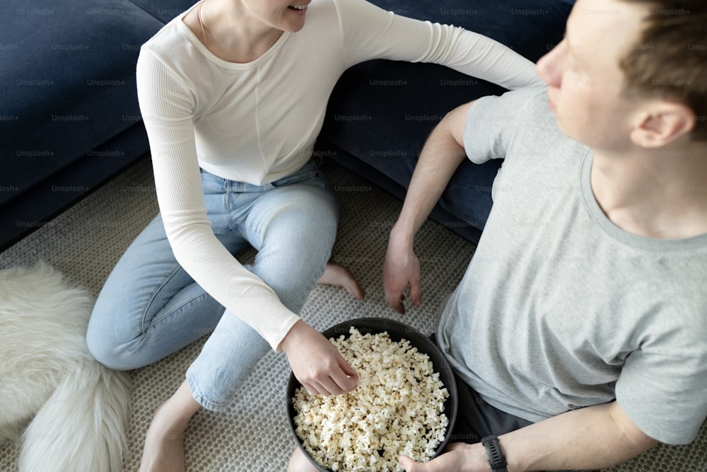 a man and a woman sitting on the floor with a bowl of popcorn