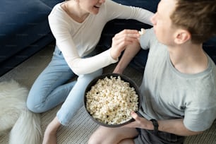a man and woman sitting on the floor eating popcorn