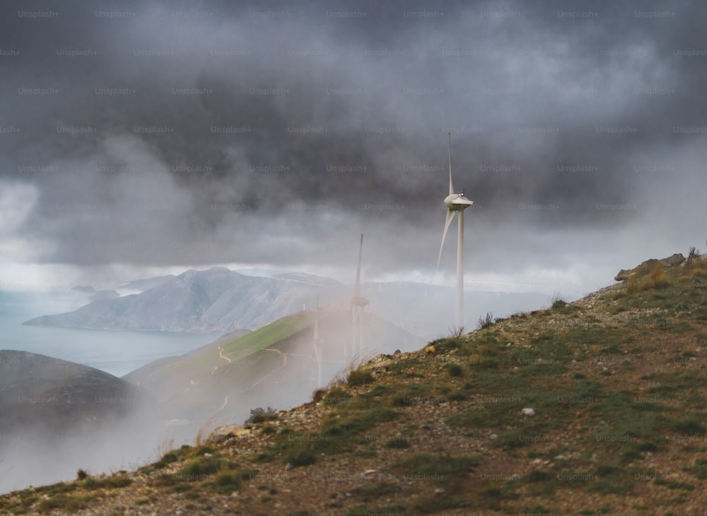 a wind turbine on a hill with a body of water in the background
