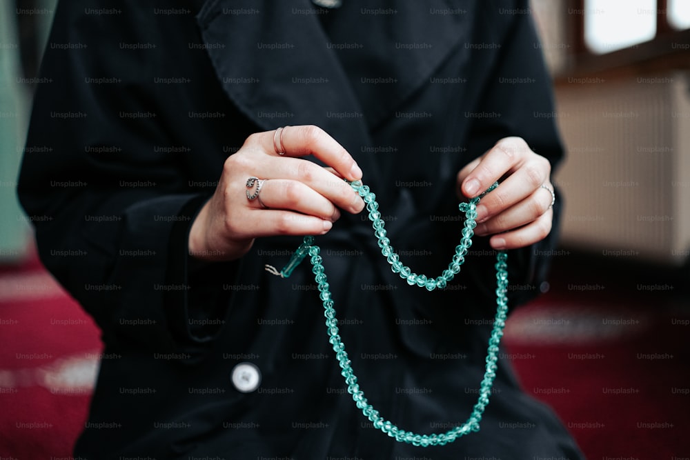 a woman wearing a black coat holding a green beaded necklace