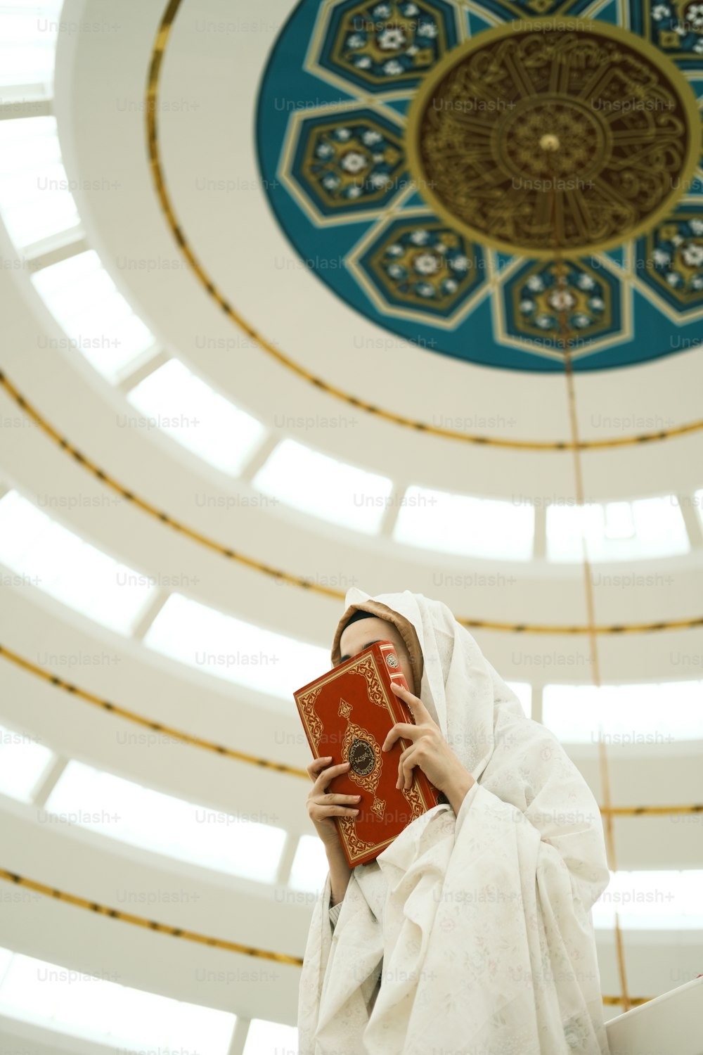 Eine Frau in einem weißen Gewand hält ein rotes Buch in der Hand