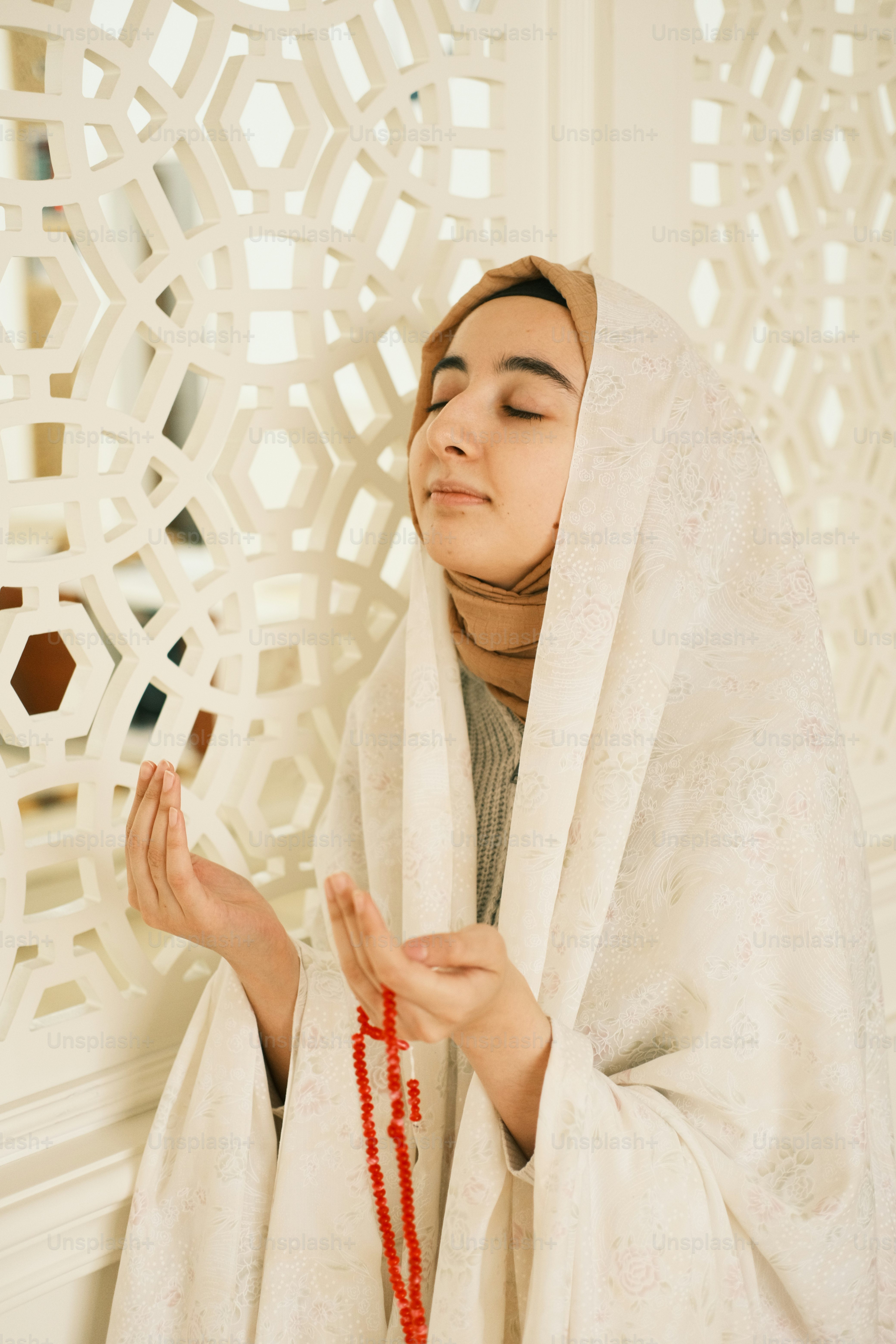 Seorang wanita mengenakan kerudung putih dan memegang kalung manik-manik merah