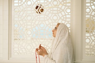 Una donna con un hijab bianco sta guardando fuori da una finestra