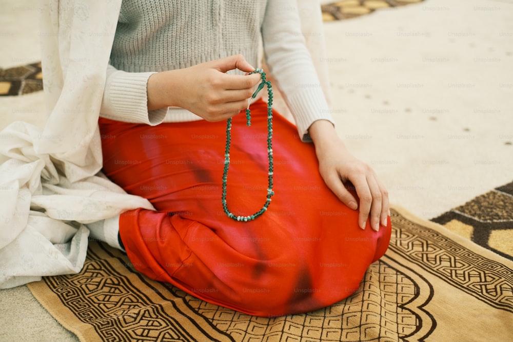 a woman sitting on a rug holding a beaded necklace