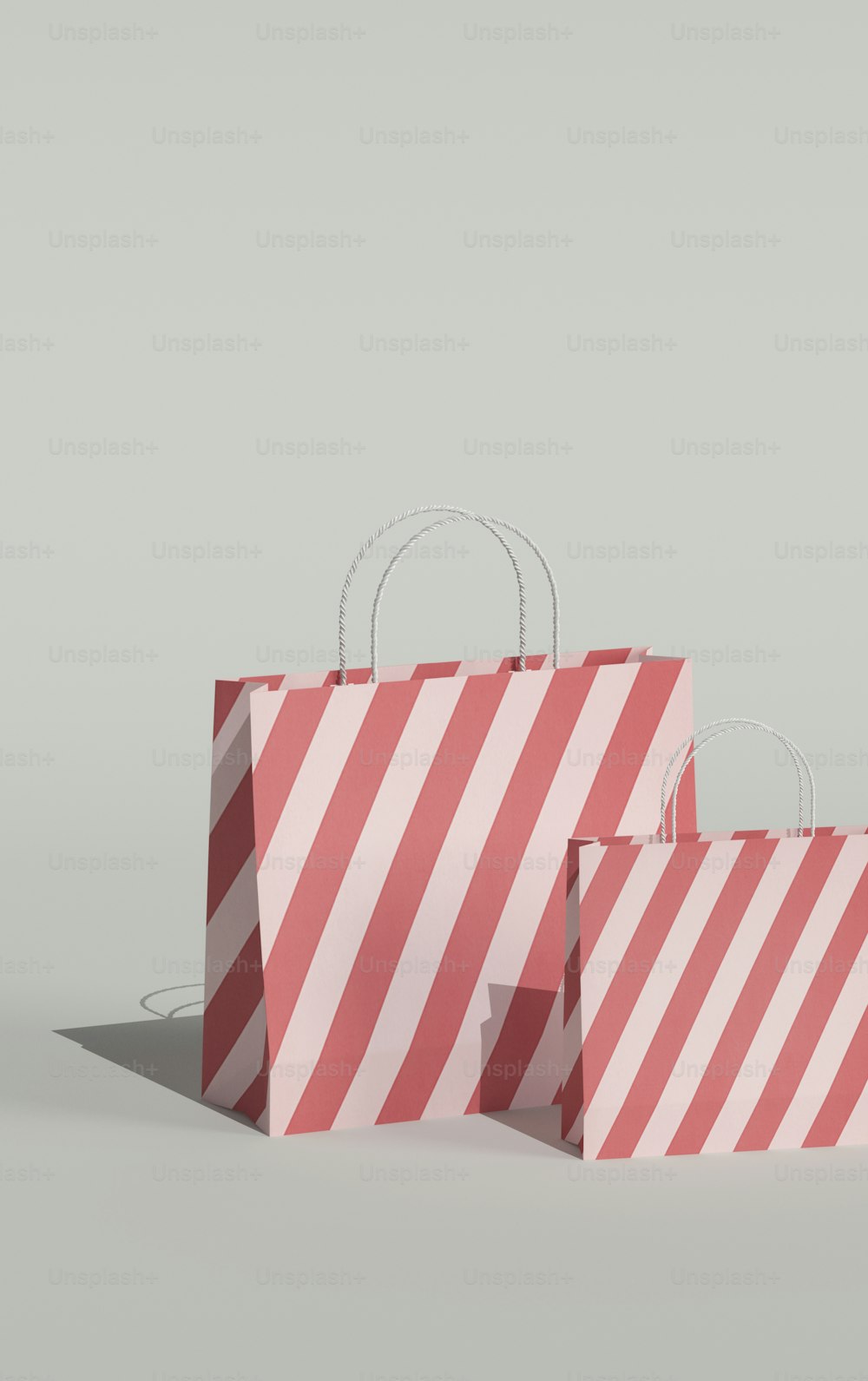 Dos bolsas de compras a rayas rojas y blancas sobre un fondo gris