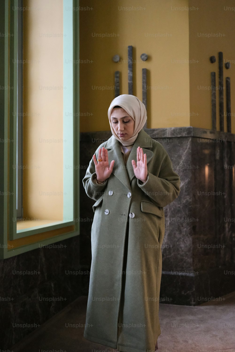a woman in a green coat standing in front of a window