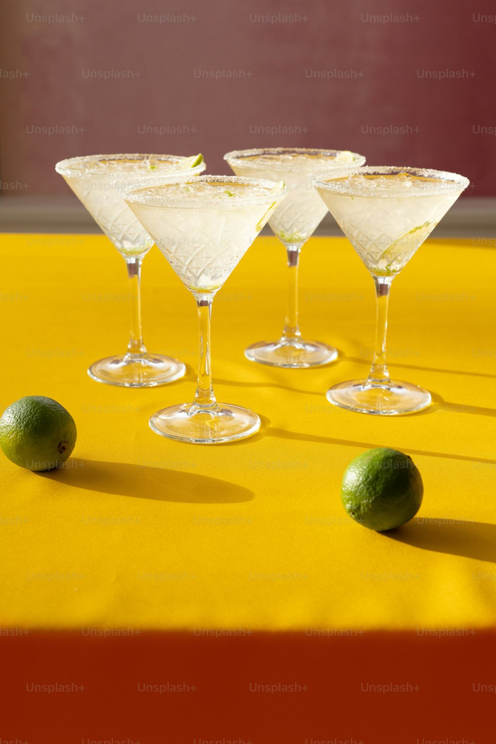 three martini glasses with limes on a yellow table