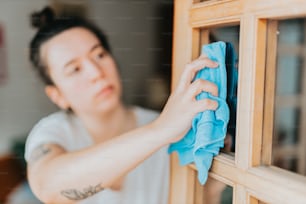 una donna che pulisce una finestra con un panno blu
