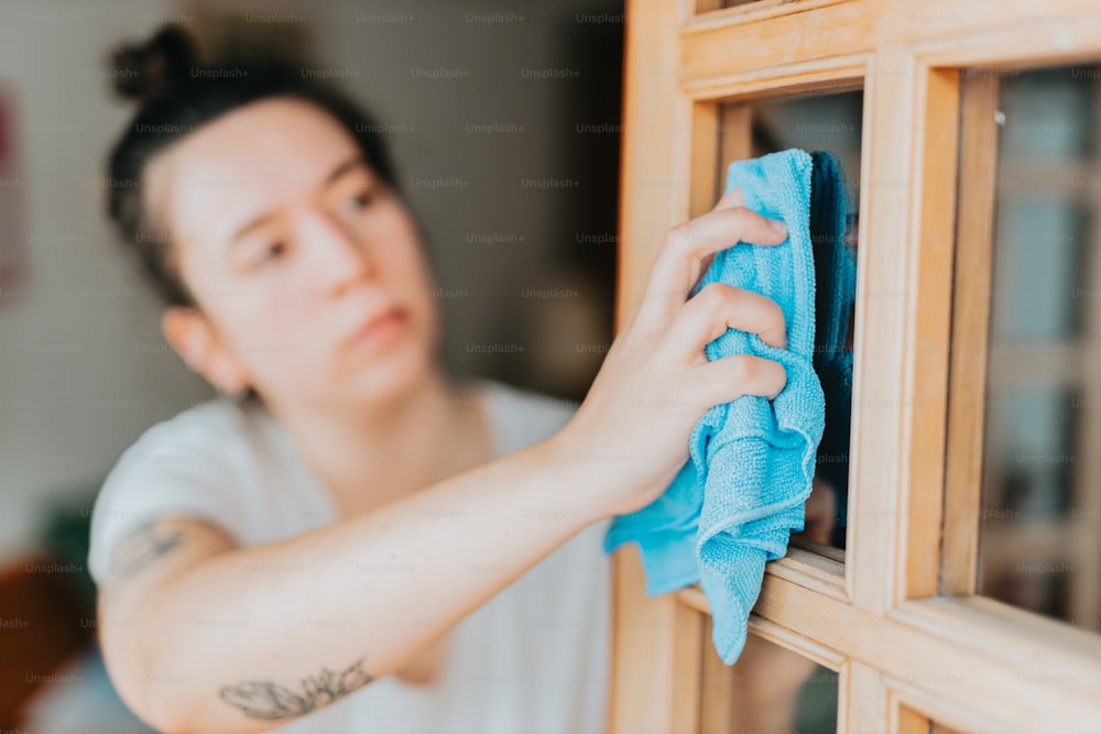 una donna che pulisce una finestra con un panno blu