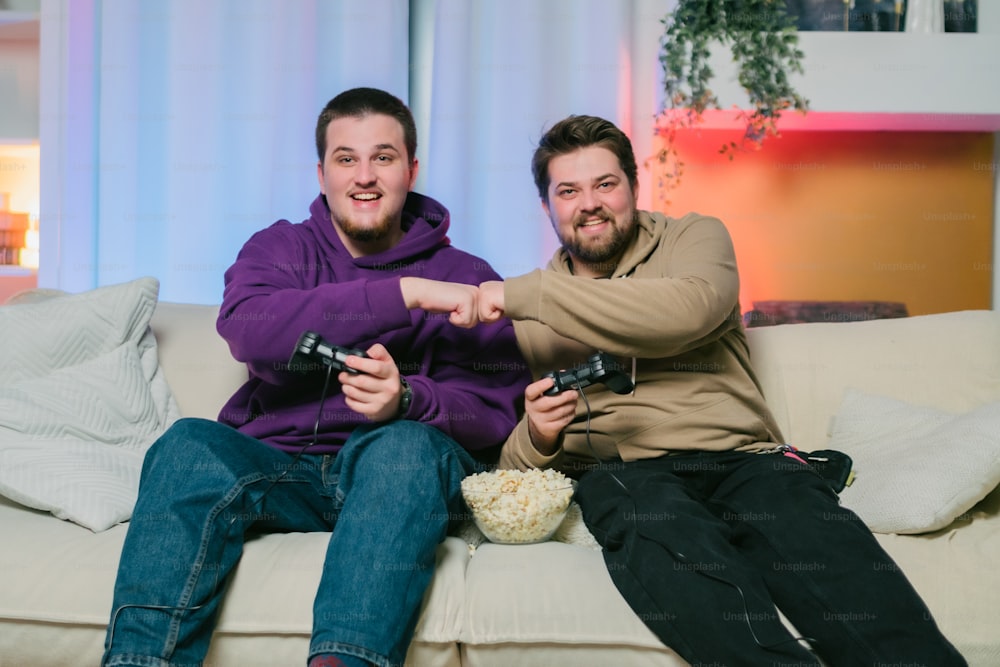 Zwei Männer sitzen auf einer Couch und spielen ein Videospiel
