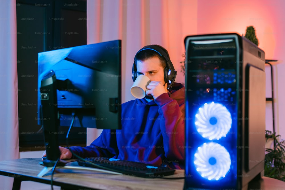 a man sitting in front of a computer drinking a cup of coffee