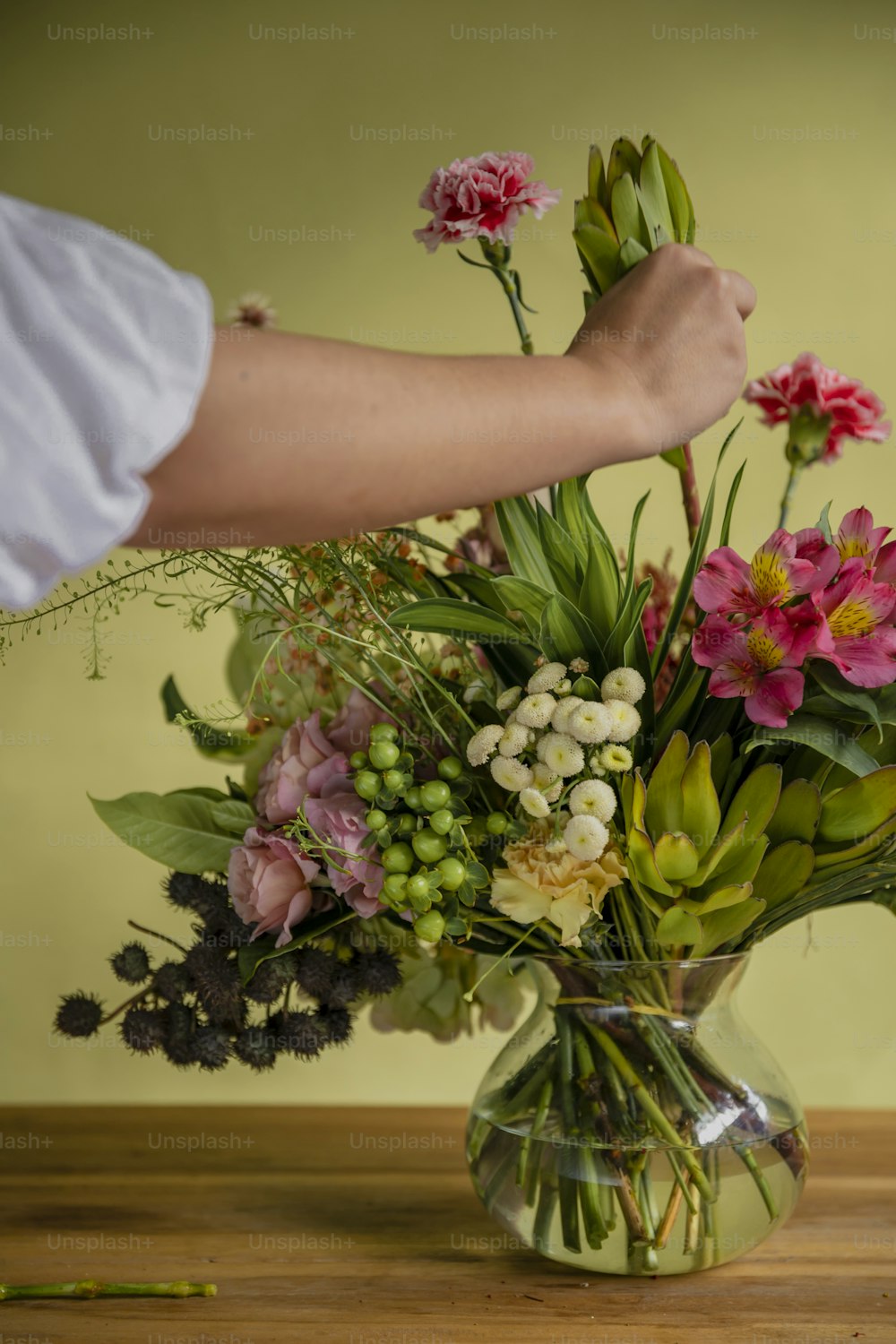 Una persona arreglando flores en un jarrón sobre una mesa