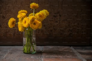 Un jarrón lleno de flores amarillas encima de un piso de piedra