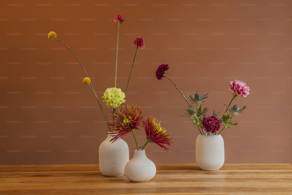 three white vases with different colored flowers in them