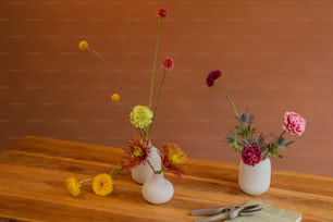 Una mesa de madera coronada con tres jarrones llenos de flores