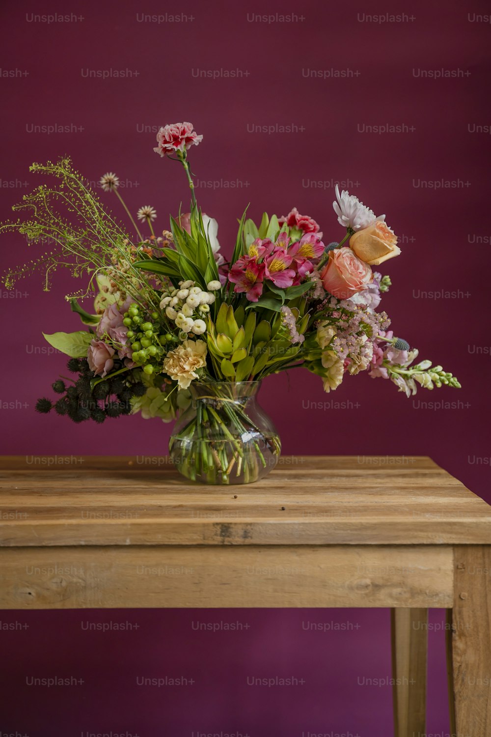 a vase filled with lots of flowers sitting on top of a wooden table