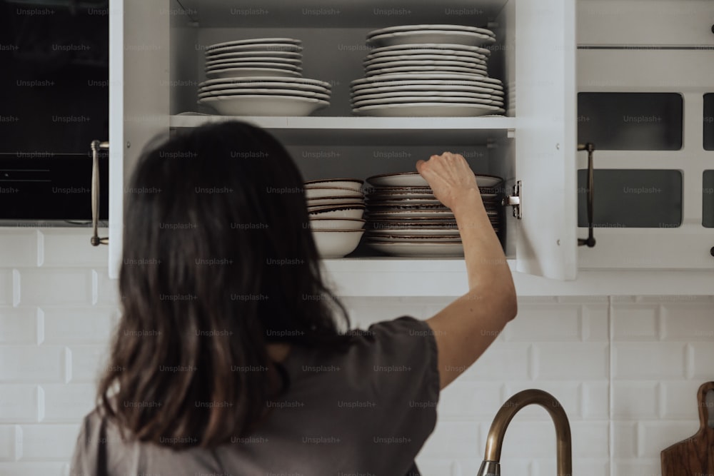 a woman is putting dishes in a cabinet
