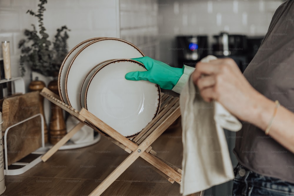 Una persona con guantes verdes limpiando platos en un estante