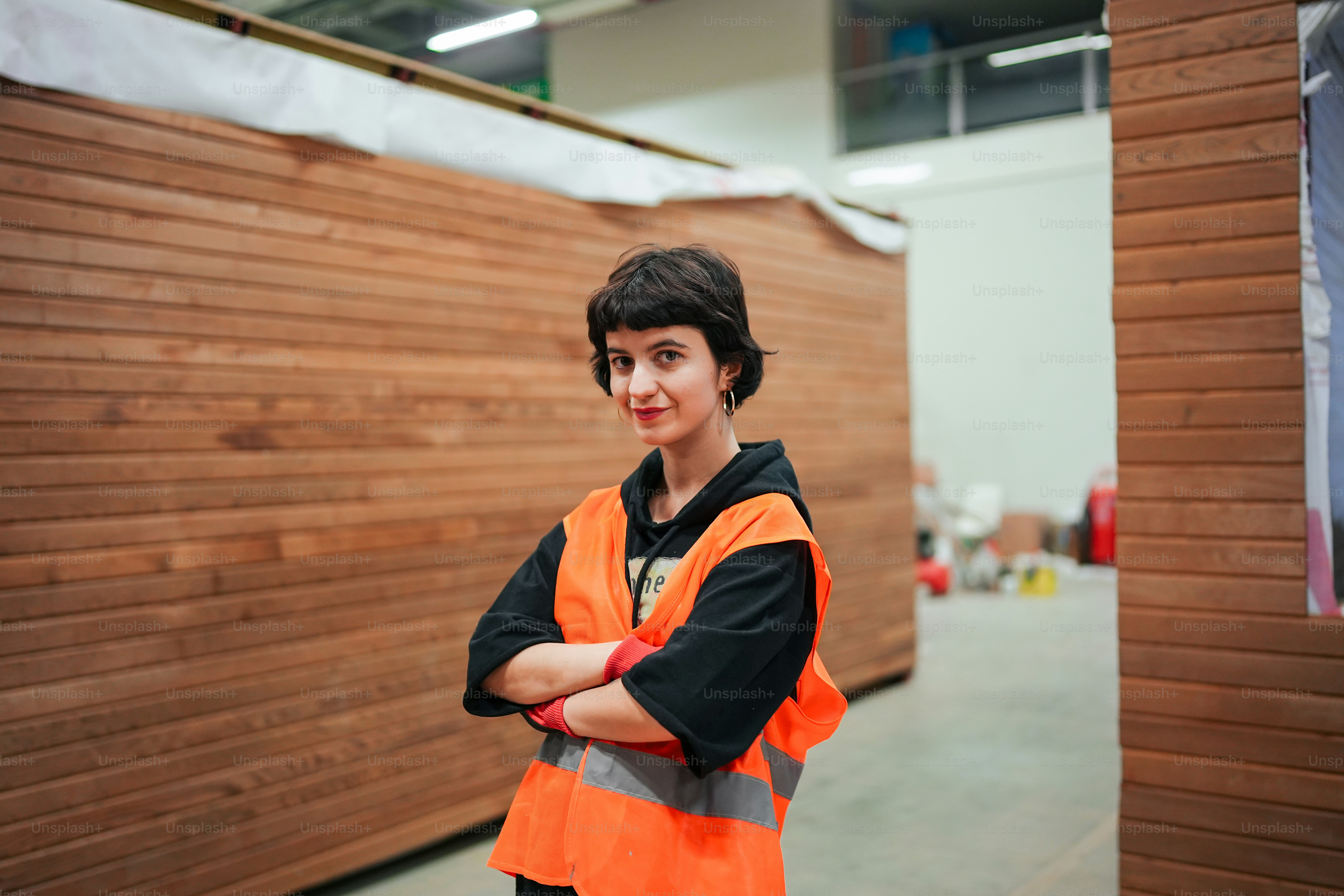 a woman in an orange vest standing in front of a wooden wall