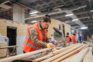 a woman in an orange vest working on a piece of wood