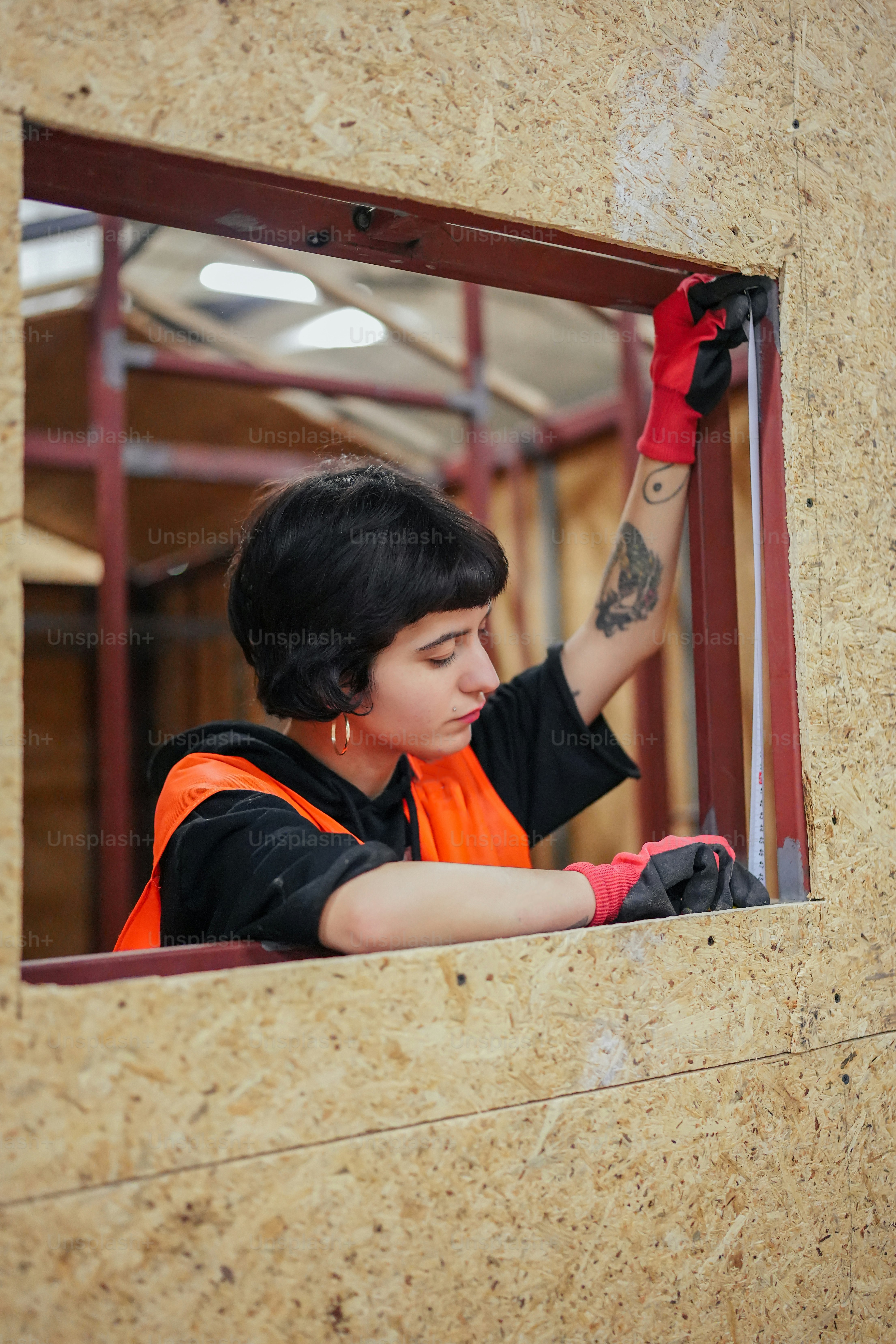 a woman in an orange vest and red gloves looking out of a window