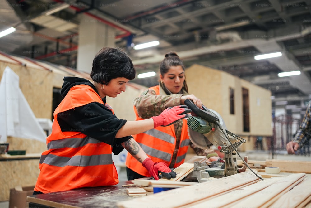 two women in orange vests working on a piece of wood