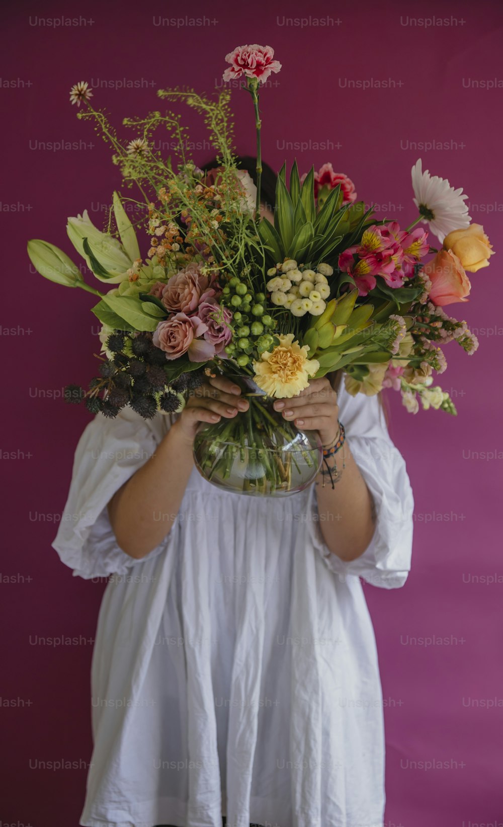 a woman holding a vase filled with lots of flowers
