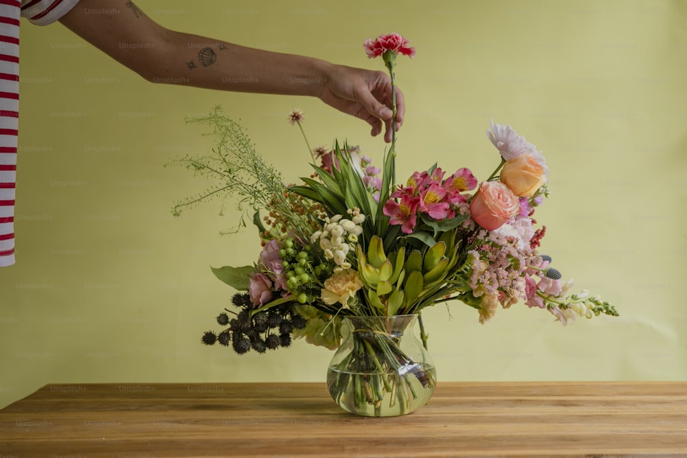 eine Person, die Blumen in einer Vase auf einem Tisch arrangiert