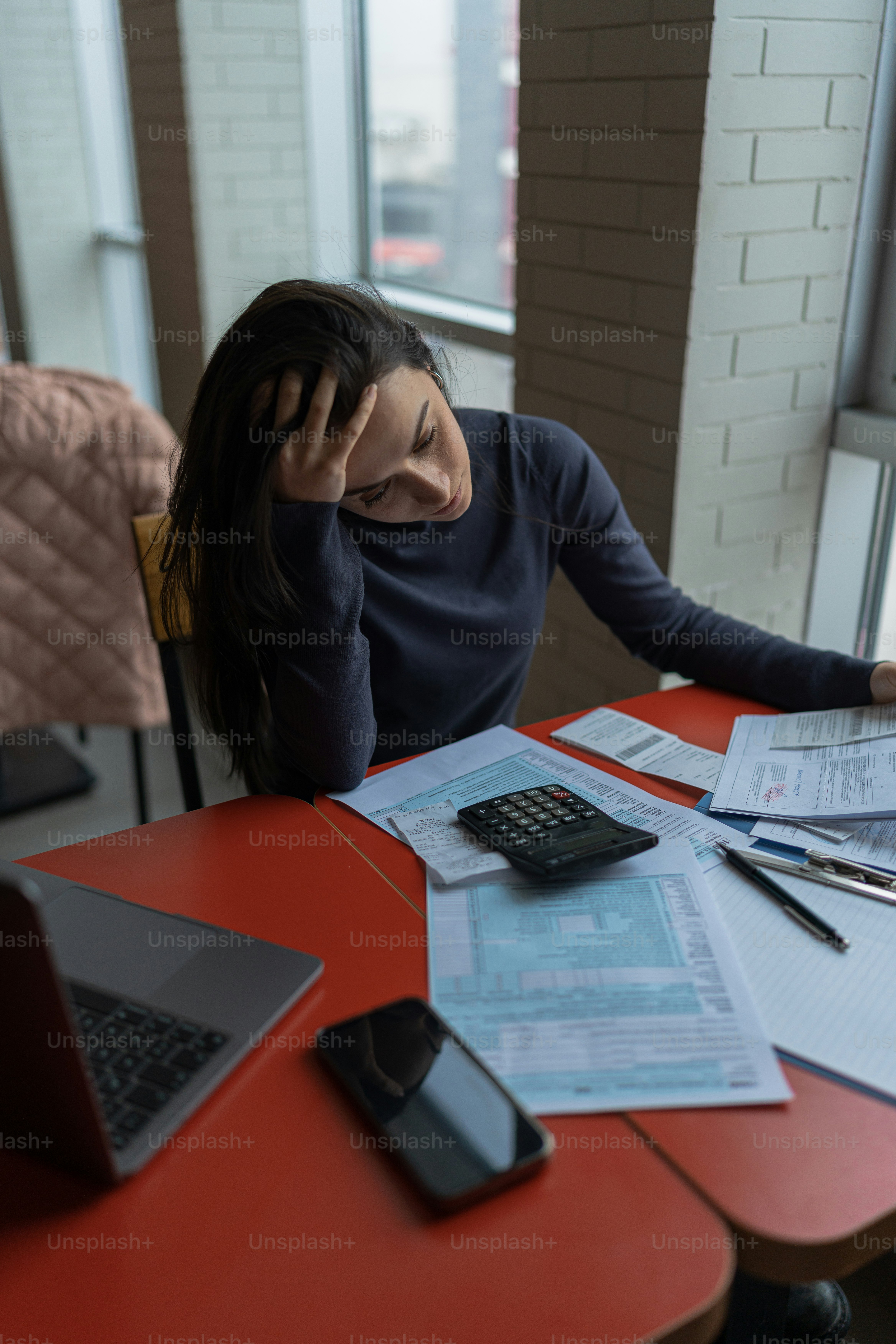 Eine Frau sitzt mit Handy und Papieren an einem Tisch
