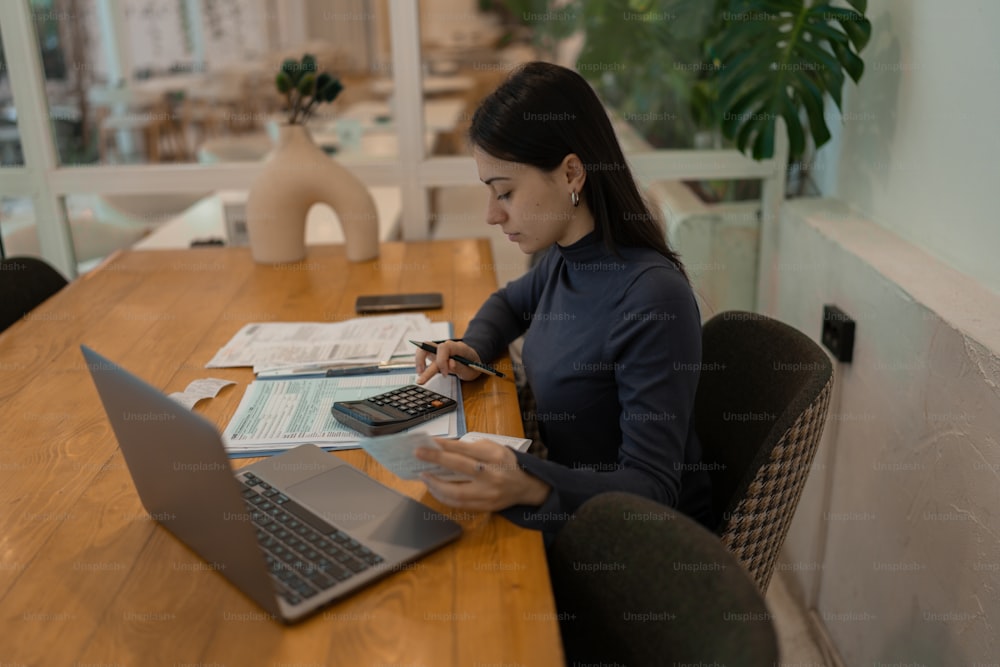 Una mujer sentada en una mesa con una computadora portátil y una calculadora