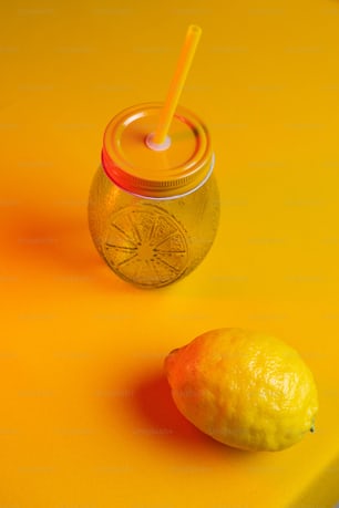 a lemon next to a jar of lemonade on a yellow surface