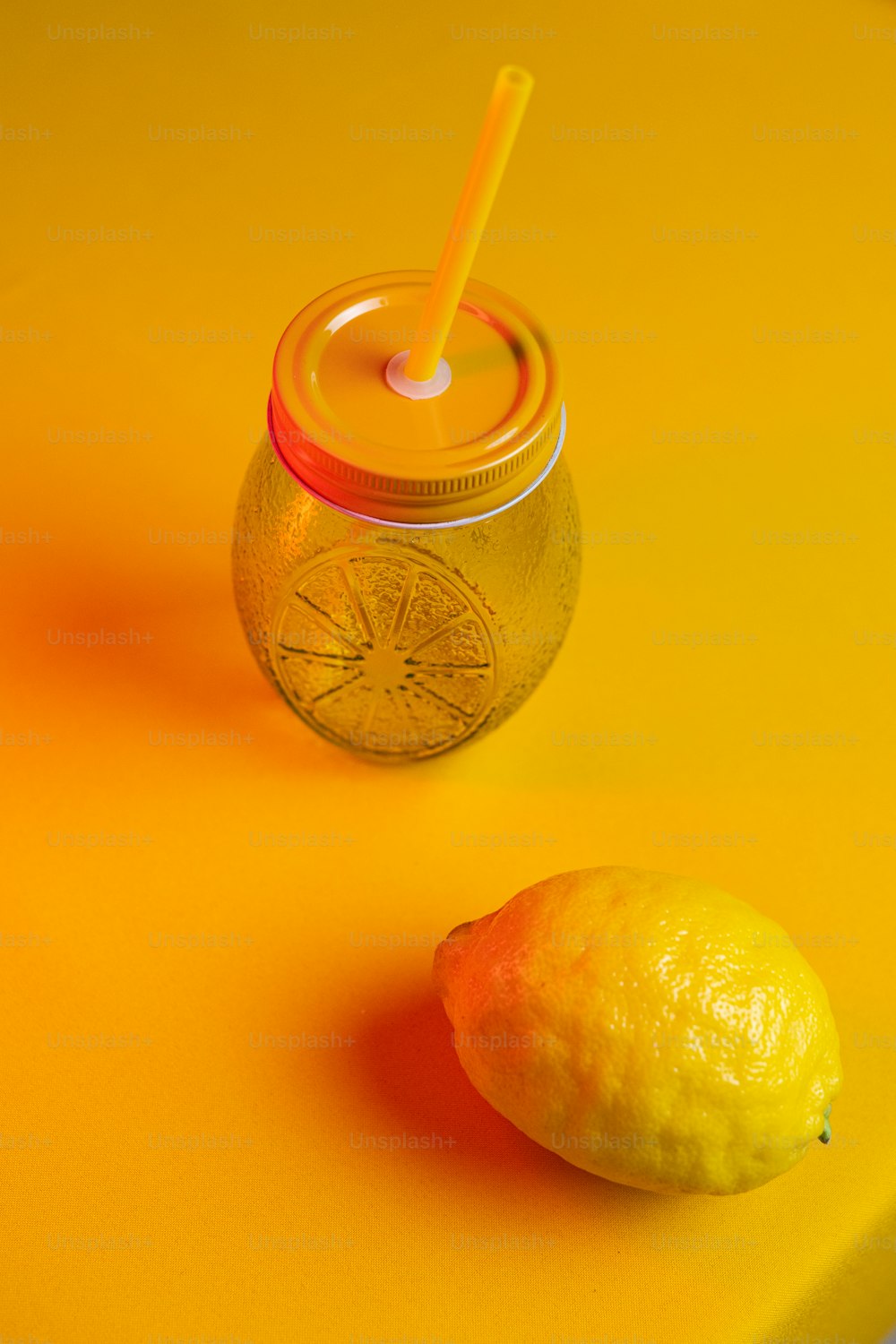 a lemon next to a jar of lemonade on a yellow surface