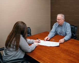 Un hombre y una mujer sentados en una mesa firmando papeles