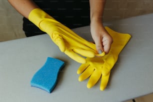 eine Person mit gelben Handschuhen und einem blauen Schwamm auf einem Tisch