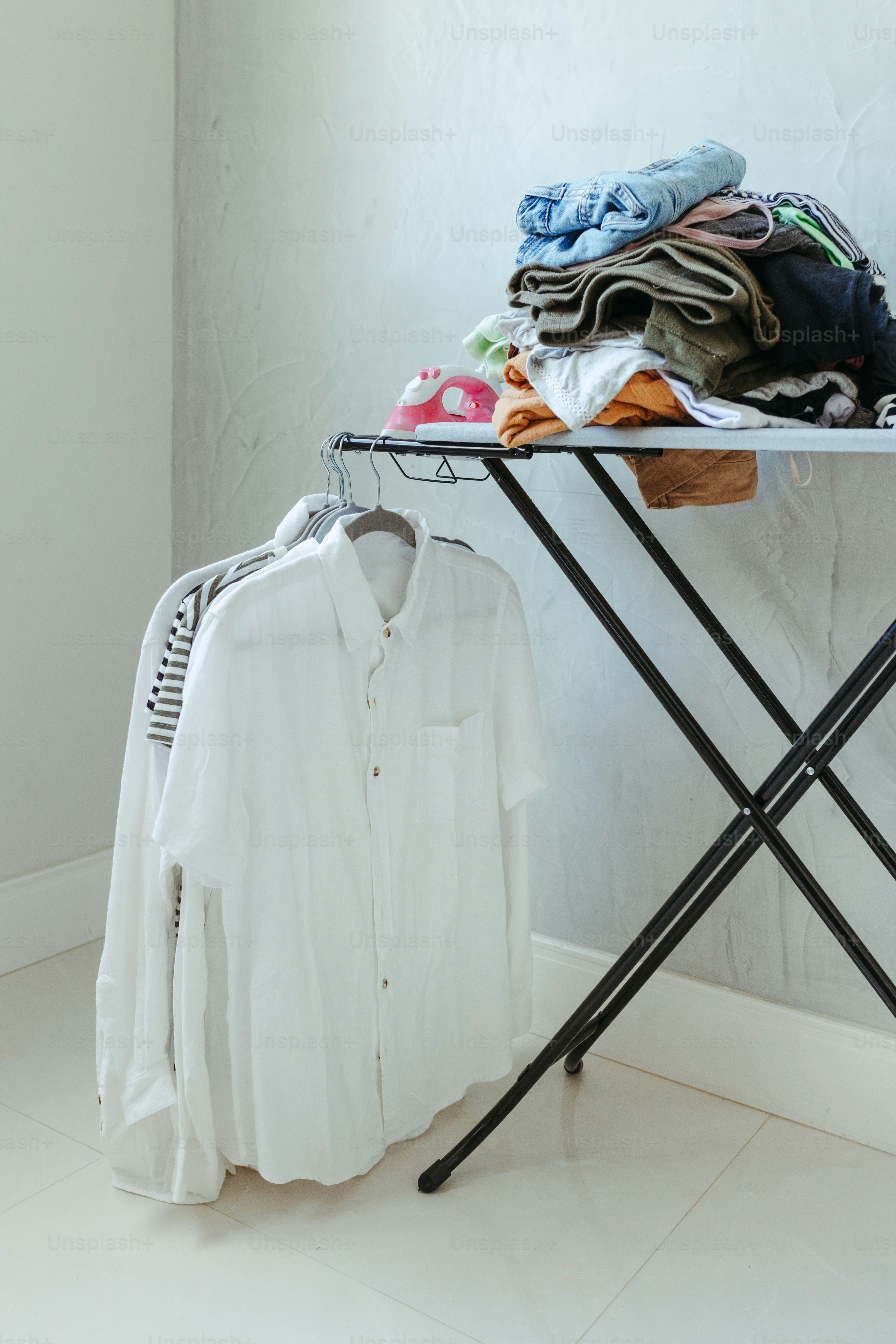 A ironing board with clothes on it next to a clothes rack photo