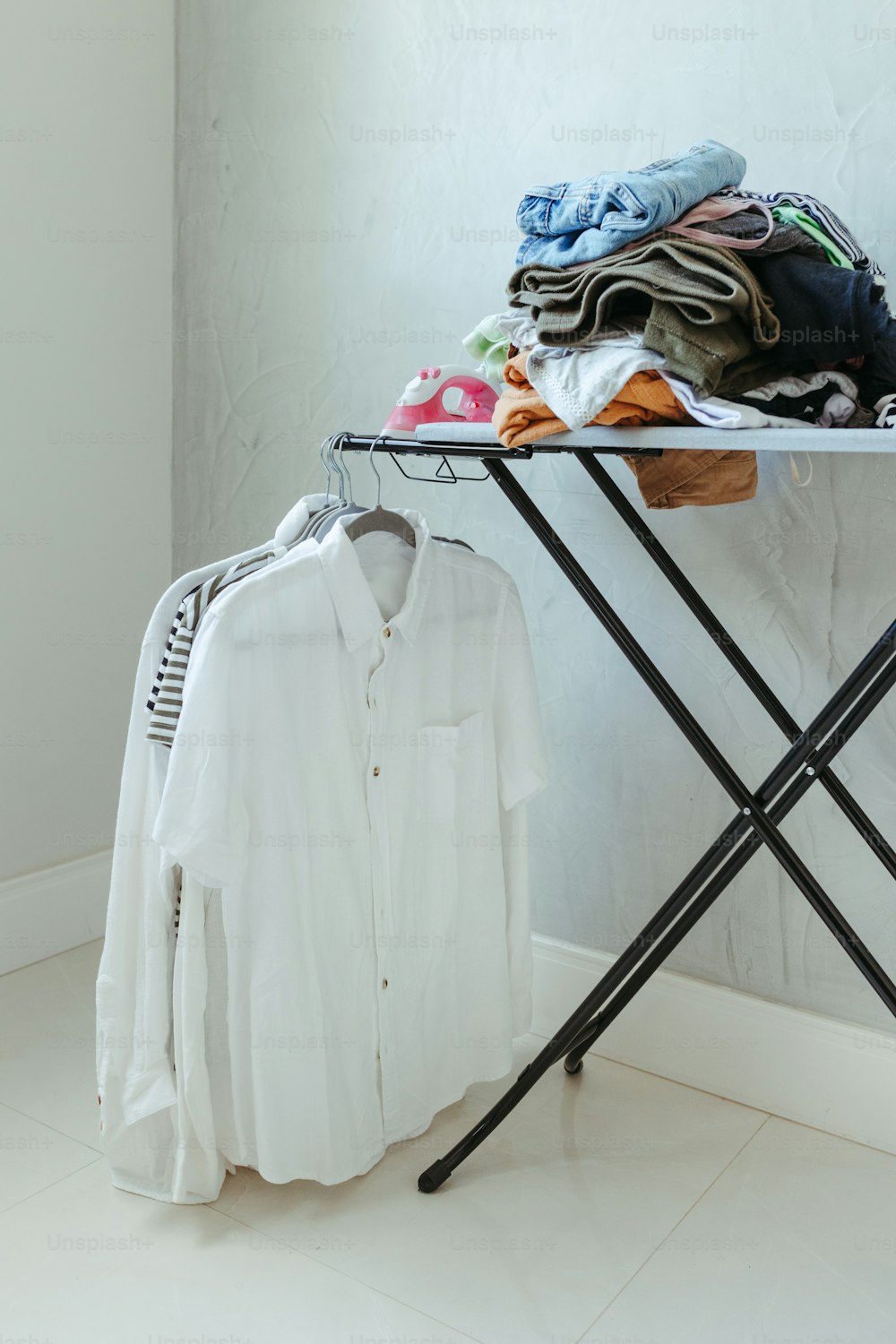 a ironing board with clothes on it next to a clothes rack