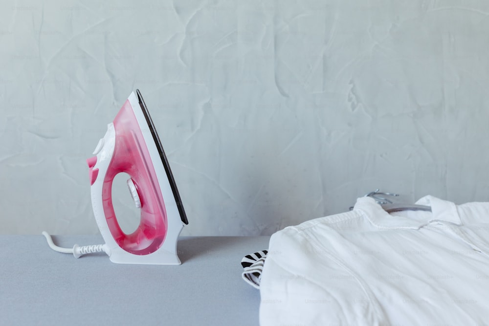 A pink and white iron sitting on top of a table photo – Laundry