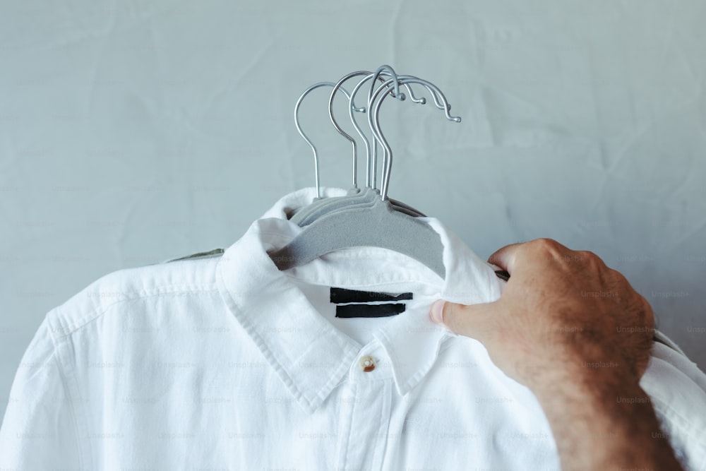 Ein Mann hält ein weißes Hemd auf einem Kleiderbügel