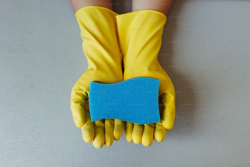 une paire de gants jaunes tenant un morceau de papier bleu